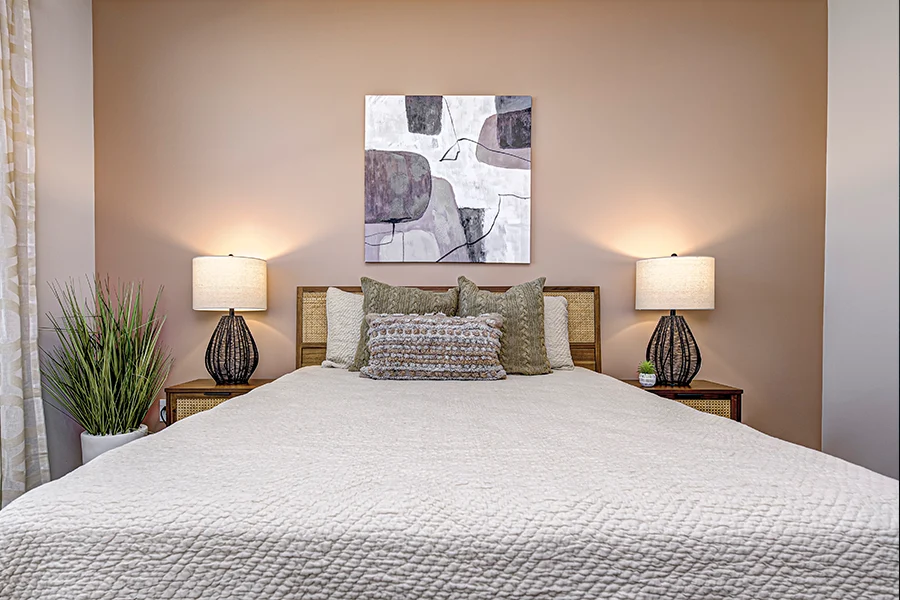 A bed styled with throw pillows, side table lamps, and artwork on the wall