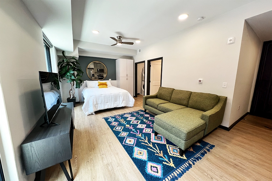 Studio apartment with colorful rug and a mirror on the wall
