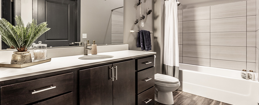 Large tiled wall with shower/tub. Dark wood cabinets. Wood plank flooring. Bathroom at Spark Apartments.