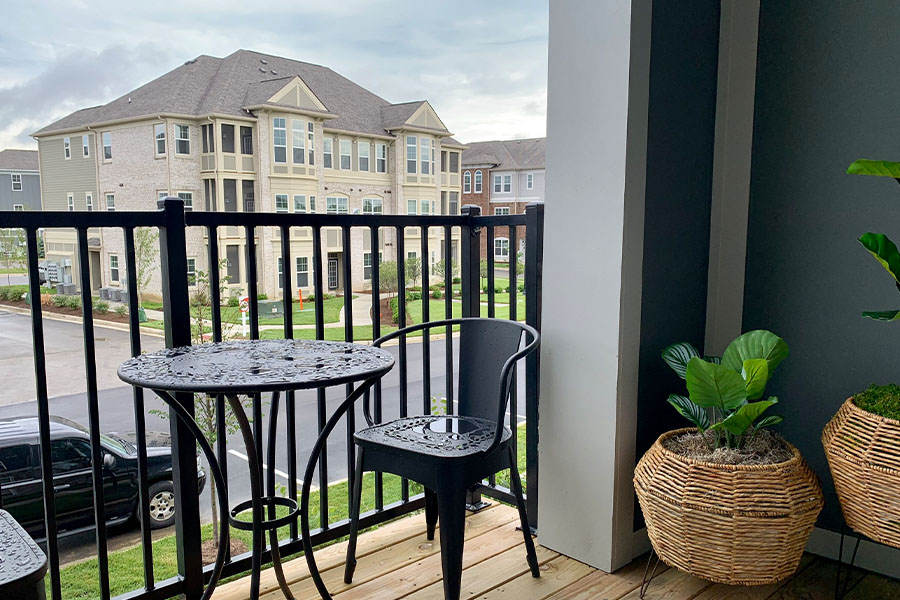 Small patio furniture gives you room to relax and move around if you have a balcony like this one at Harmony Apartments. Small black patio iron table and chairs on an upper-level patio with potted plants. Located at Harmony Apartments.